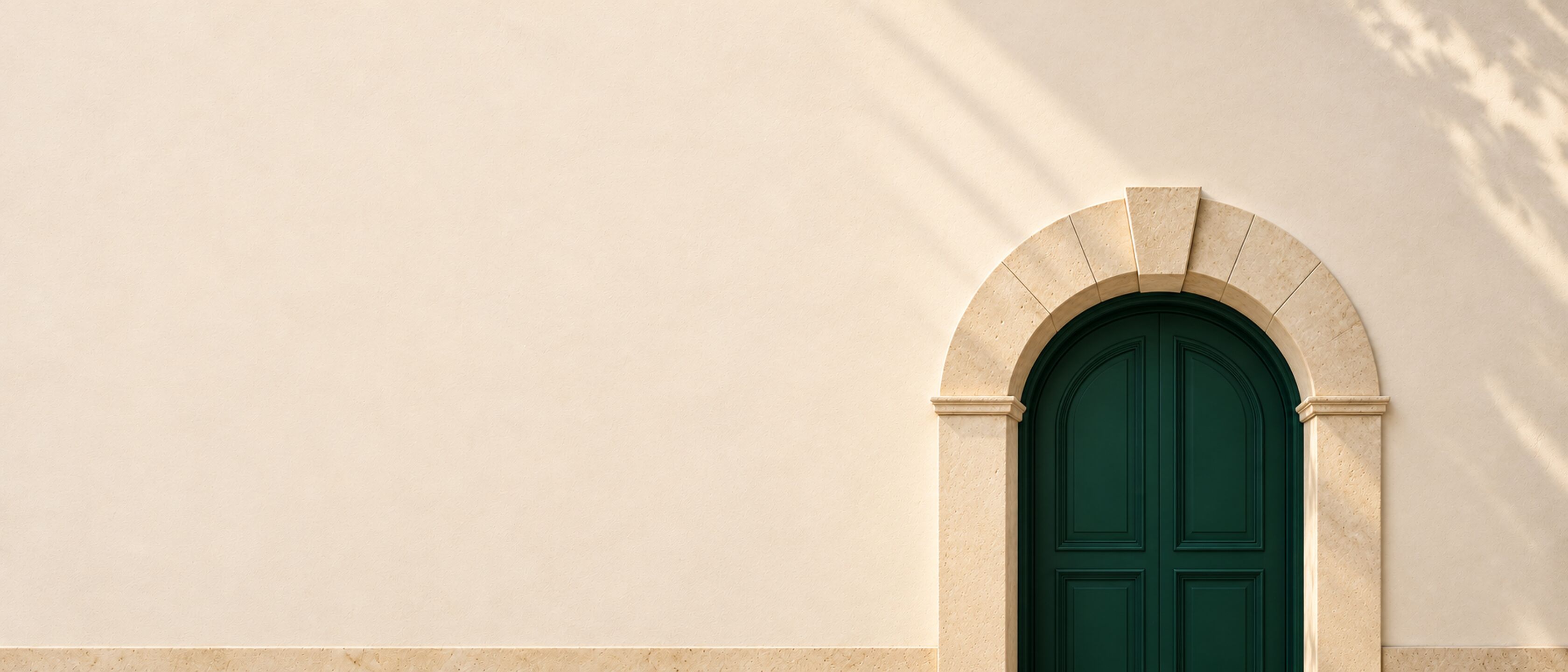 Warm ivory plaster wall with a limestone arch and prominent keystone above forest-green panelled double doors
